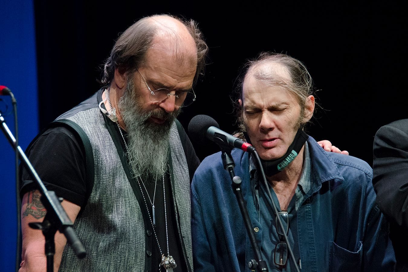 Steve Earle has his left arm around Malcolm Holcombe on stage.